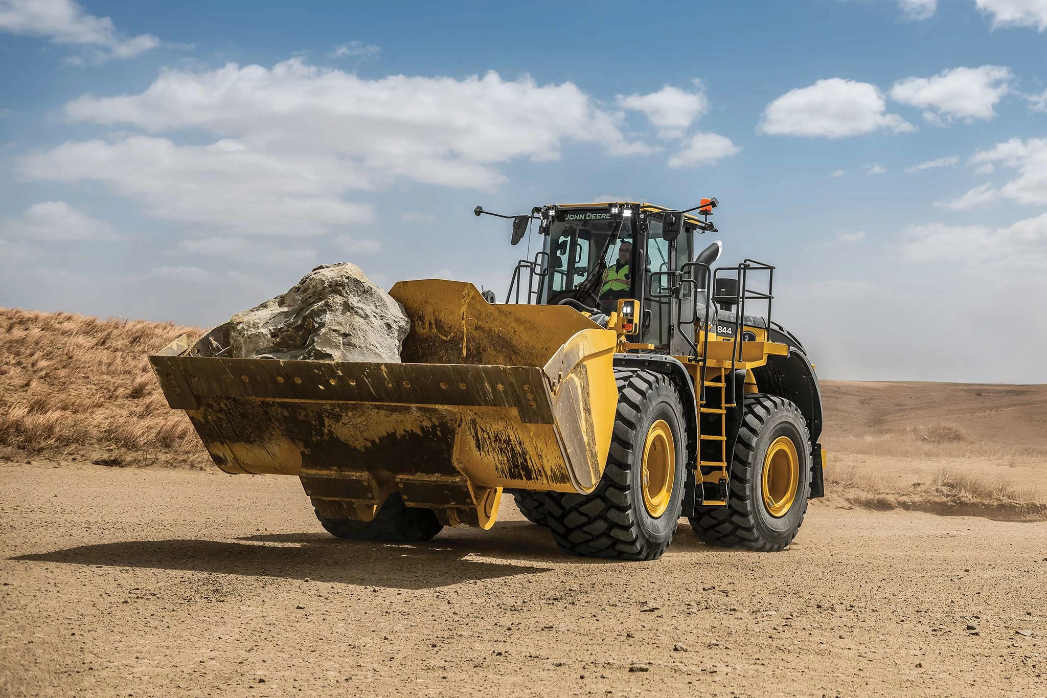 Front left view of an 844 X-Tier wheel loader on a dirt lot with a boulder in its front bucket