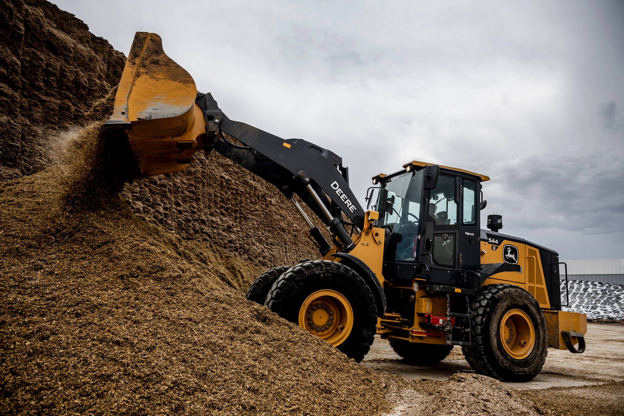 Side left view of a 544G Wheeled Loader pushing material atop a large pile