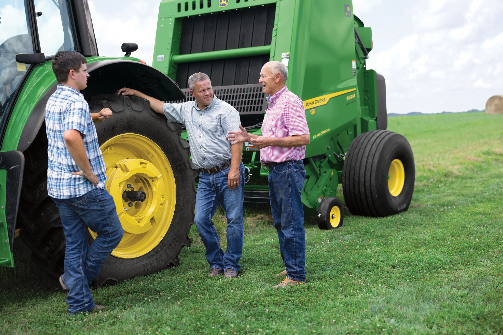 Farmers discussing their John Deere round baler in the field