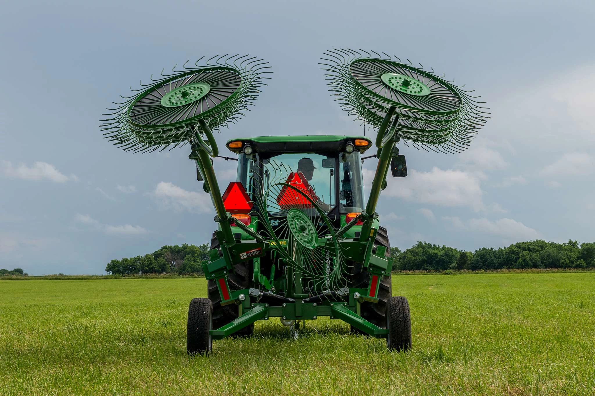 Rear view of a tractor with attached WR00 series wheel rake, wheels folded above in transport mode