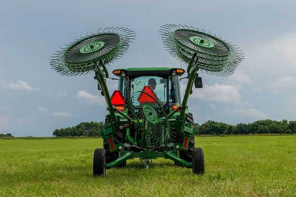 Rear view of a tractor with attached WR00 series wheel rake, wheels folded above in transport mode