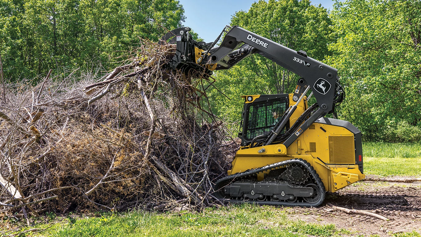 333 P-Tier compact track loader using a grapple attachment to clear a pile of branches.