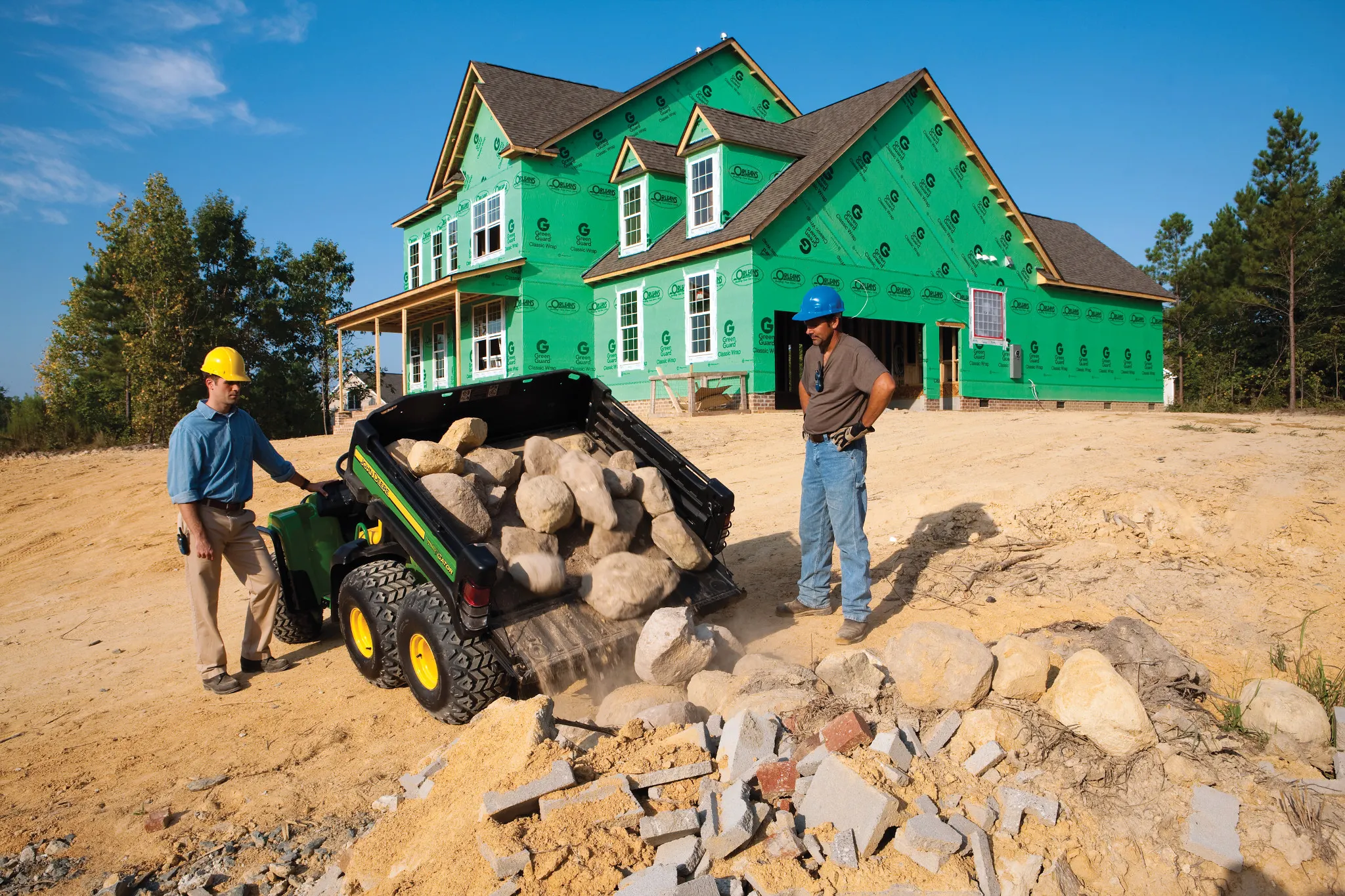 Men in construction hats operate a Gator TH 6x4 dumping rocks in the field