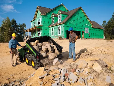 Men in construction hats operate a Gator TH 6x4 dumping rocks in the field