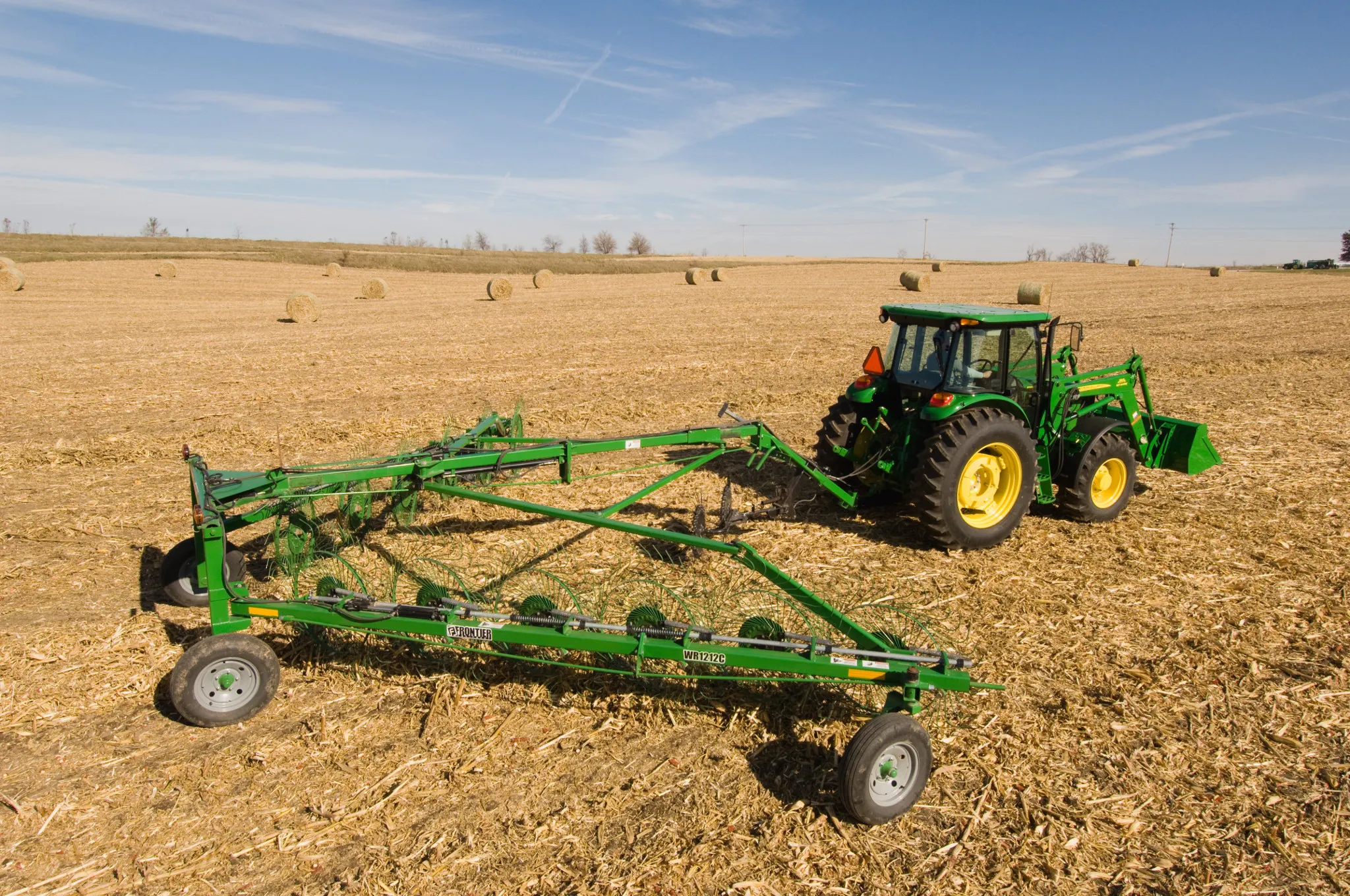 Side right view of a green John Deere tractor pulling a WR1212 High-Capacity Wheel Rake across a harvested field