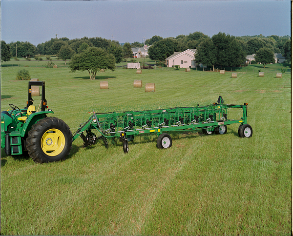 Tractor pulling a long wheel rake across a grassy field with multiple round hay bales scattered in the background