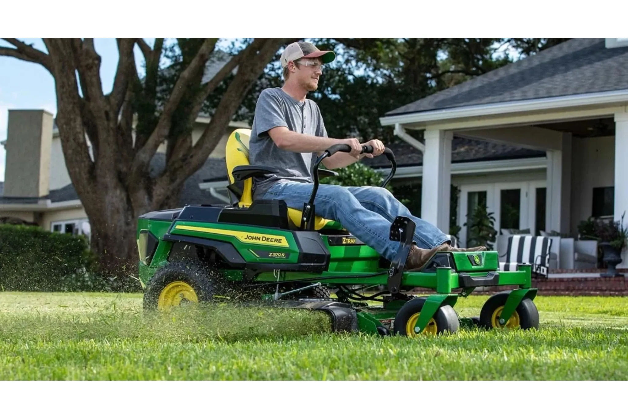 A farmer riding on a green lawn mower in front of a house