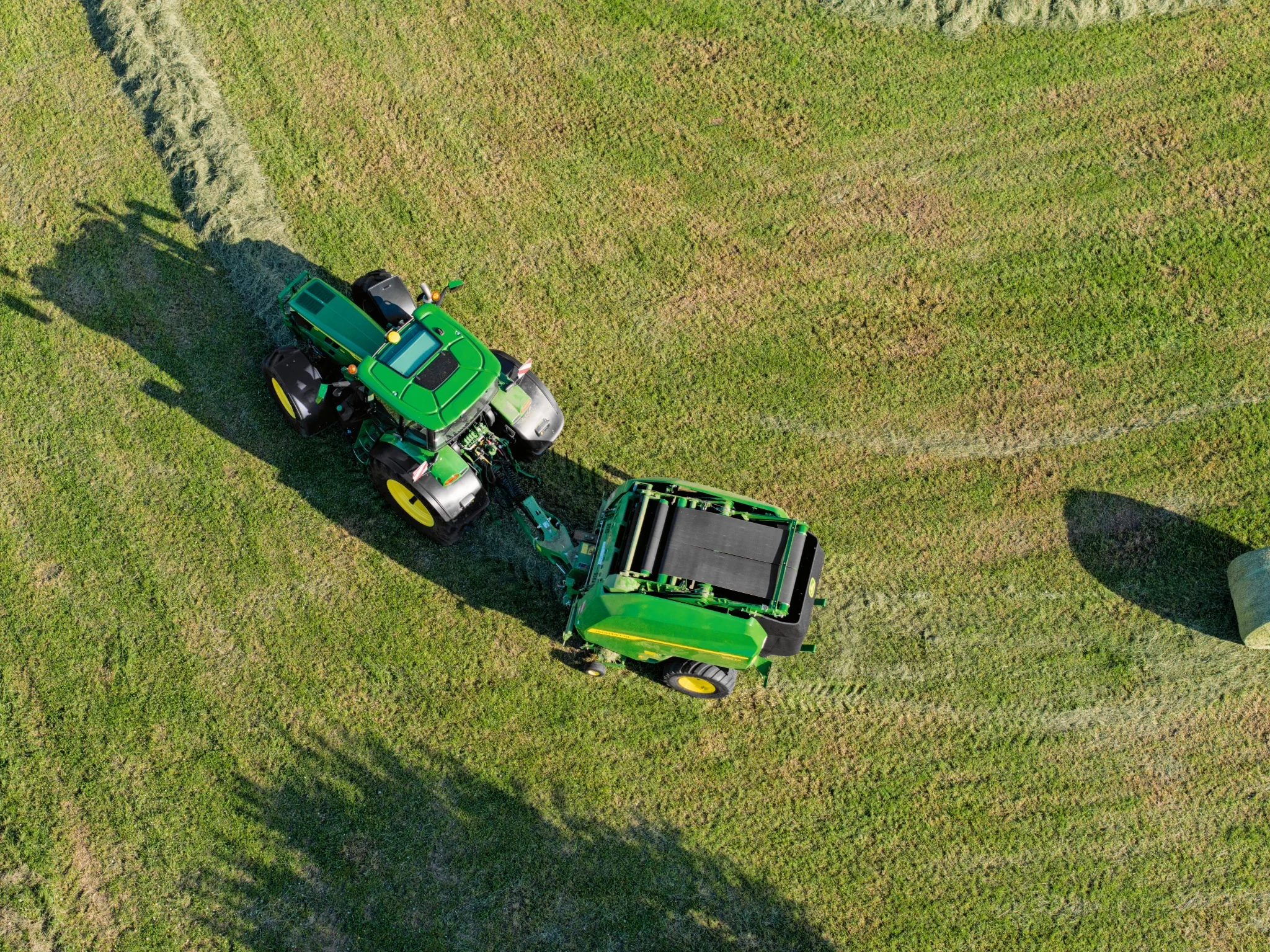 Aerial view of a tractor and baler rounding a corner in a green field