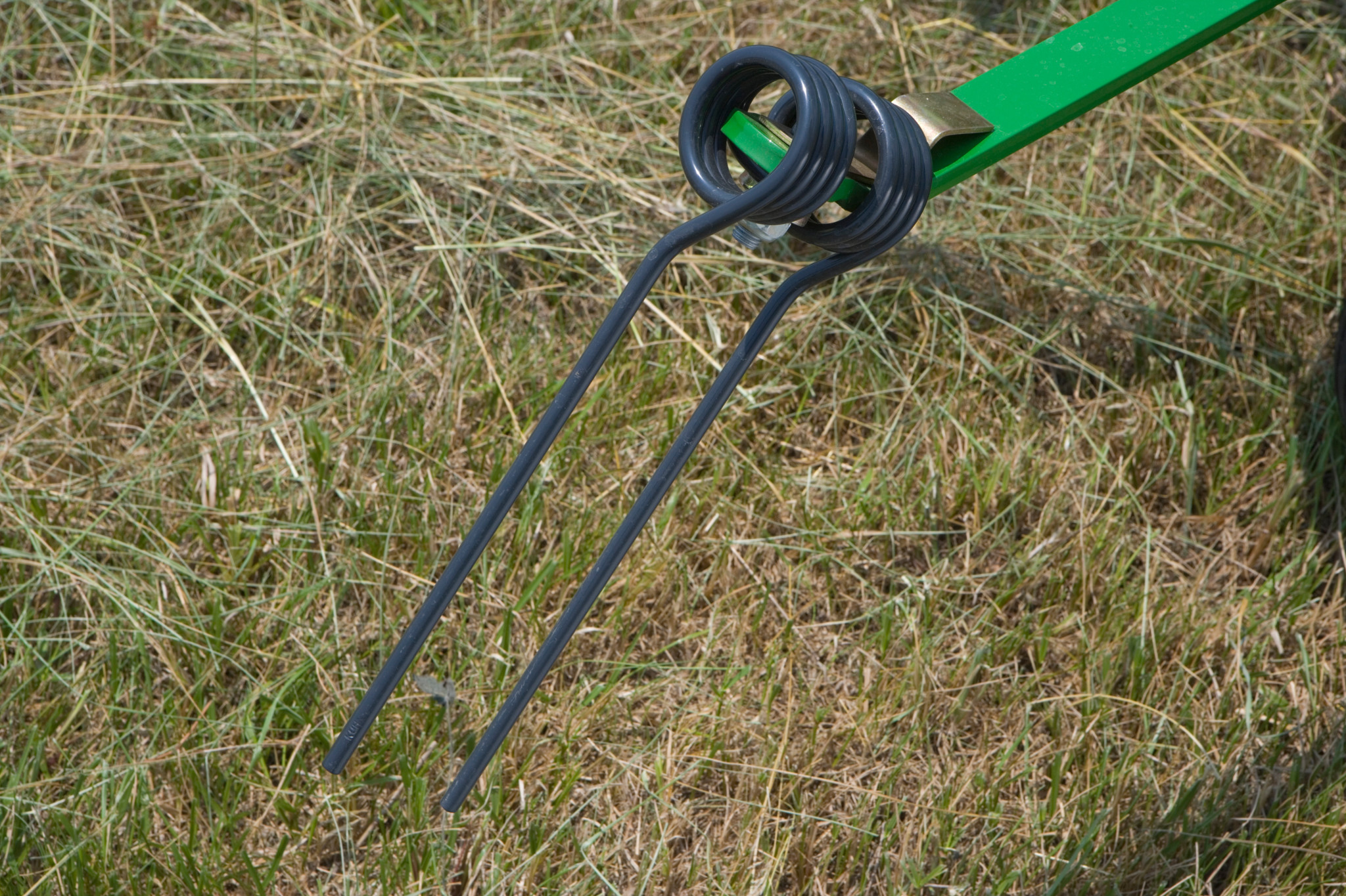 Steel tine on a hay tedder pulling cut grass in a field