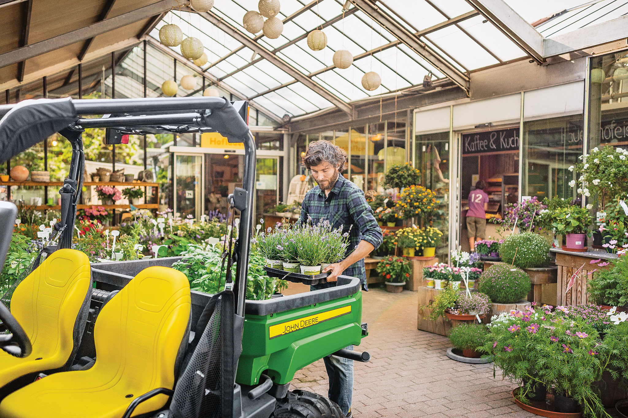 View from the left front of an XUV560E Crossover Utility Vehicle of a man loading the cargo box with herbs inside a greenhouse
