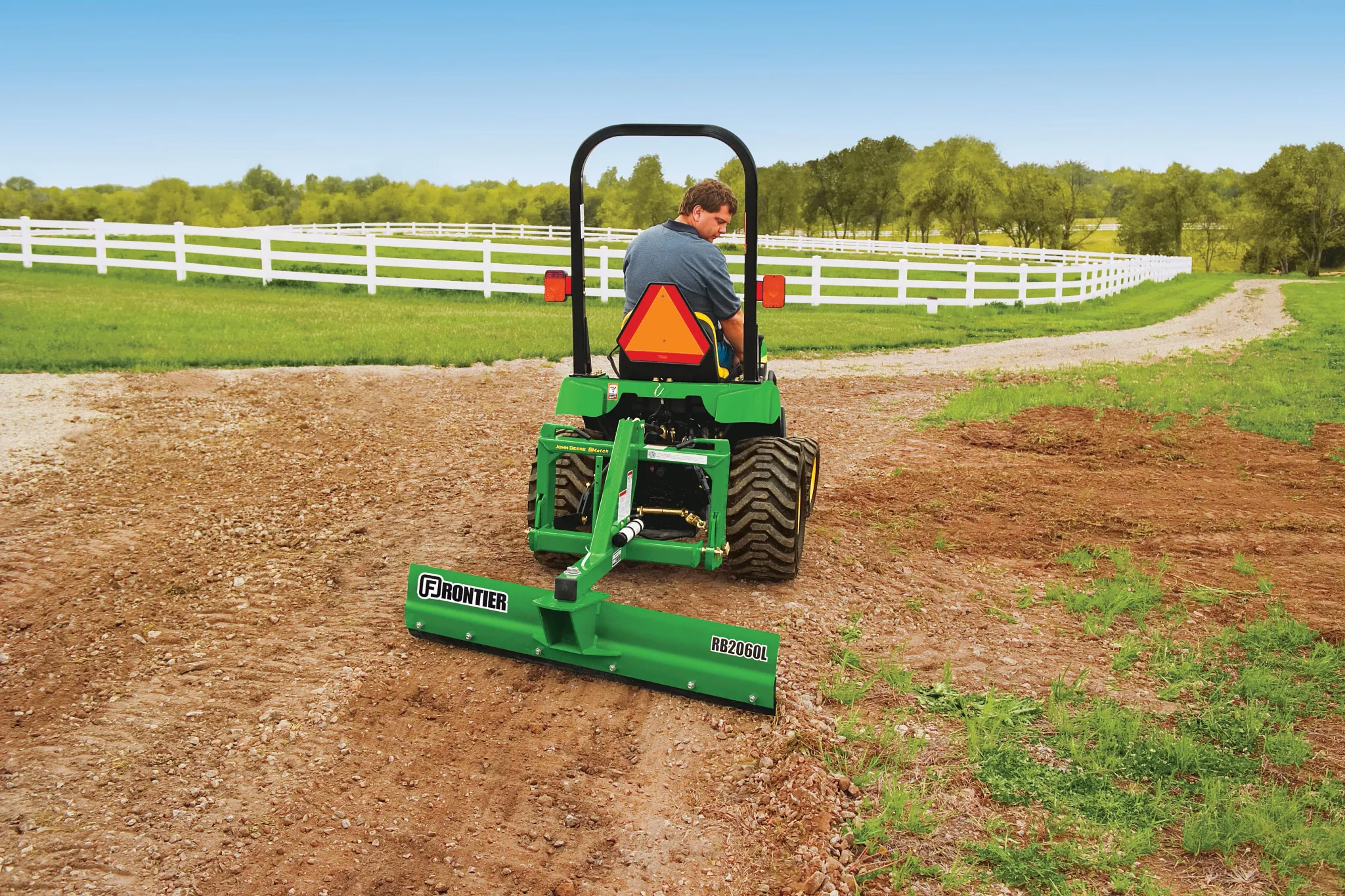 Rear view of a tractor on a farm path using a green, rear-attached RB2060L Rear Blade