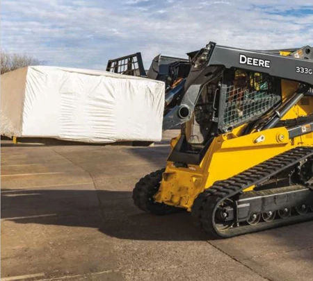 Side left view of a 333G Skid Steer with PF-Series pallet forks attachment hauling a pallet in a parking lot