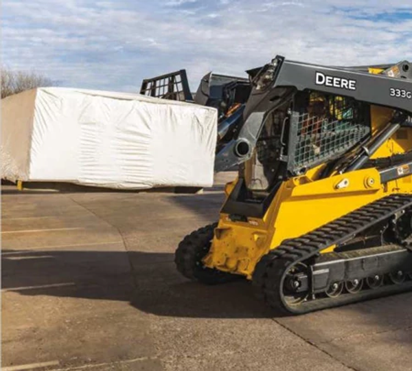 Side left view of a 333G Skid Steer with PF-Series pallet forks attachment hauling a pallet in a parking lot