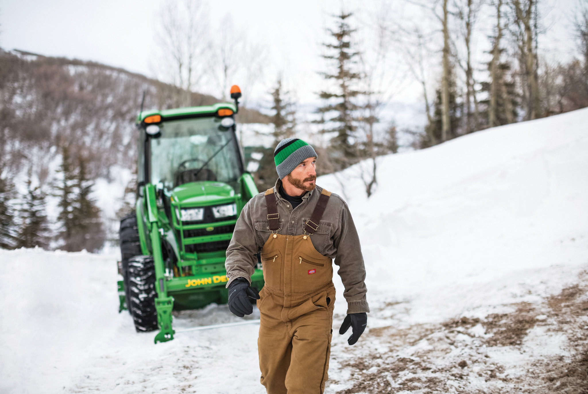 Owner beside a John Deere 4066R cab tractor in a snowy landscape