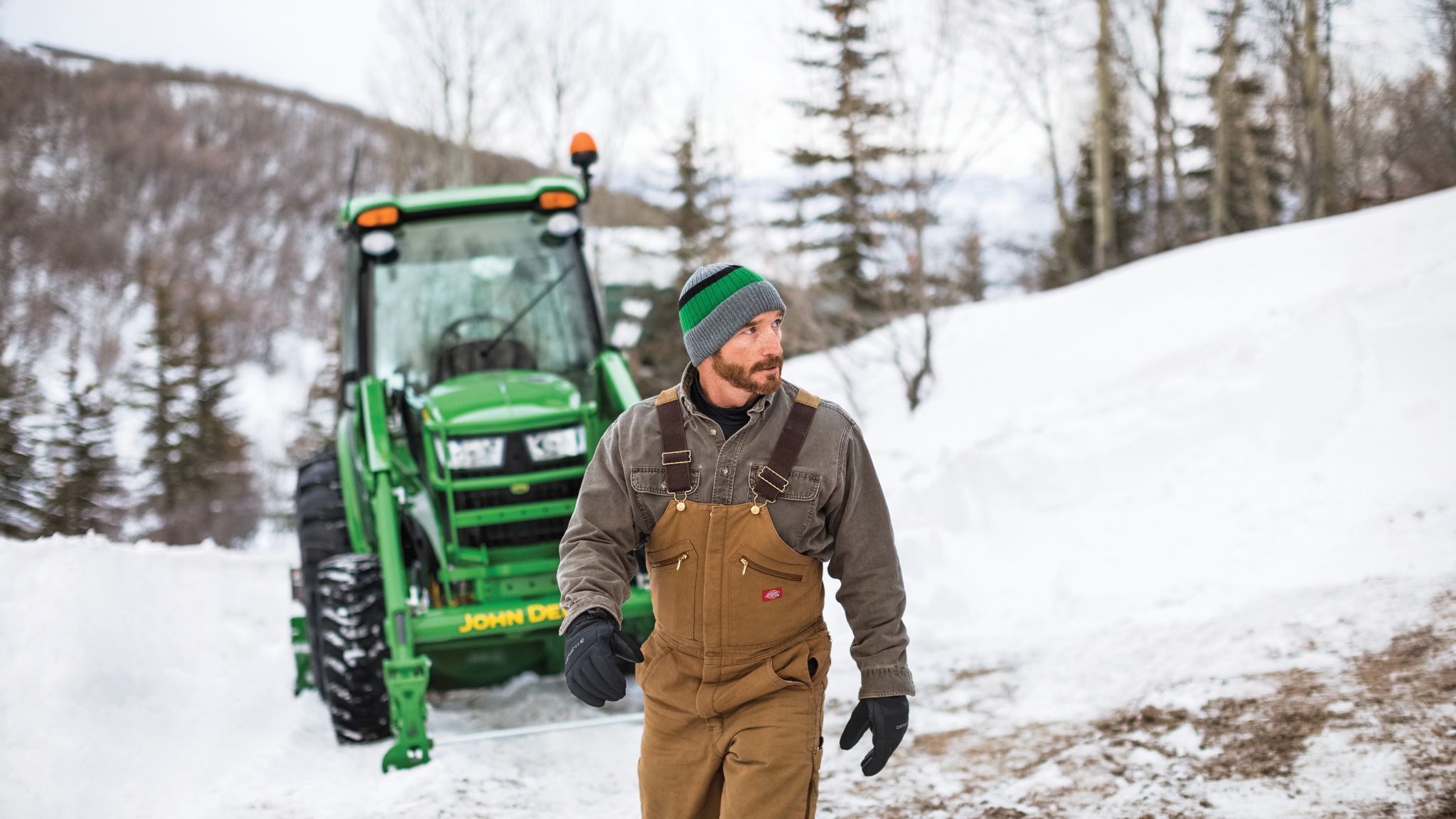 Owner beside a John Deere 4066R cab tractor in a snowy landscape