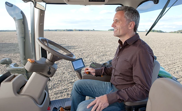 Smiling man sits in cab of tractor in field