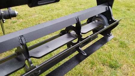 Front view of the end of a tillage ripper's black internal basket scraper with grass in the background