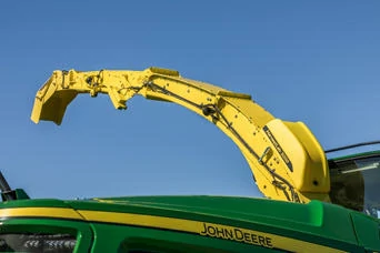 HarvestLab 3000 mounted on a ellow discharge spout on top of a green forage harvester, shown against a clear blue sky