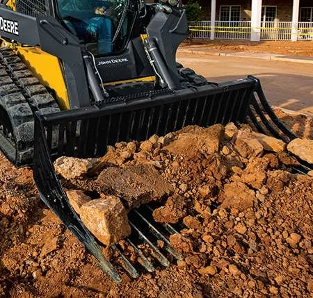 Close-up front angled view of a rock bucket attachment sifting rocks from dirt on a residential jobsite.