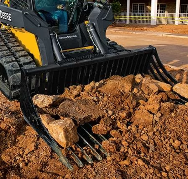 Close-up front angled view of a rock bucket attachment sifting rocks from dirt on a residential jobsite.
