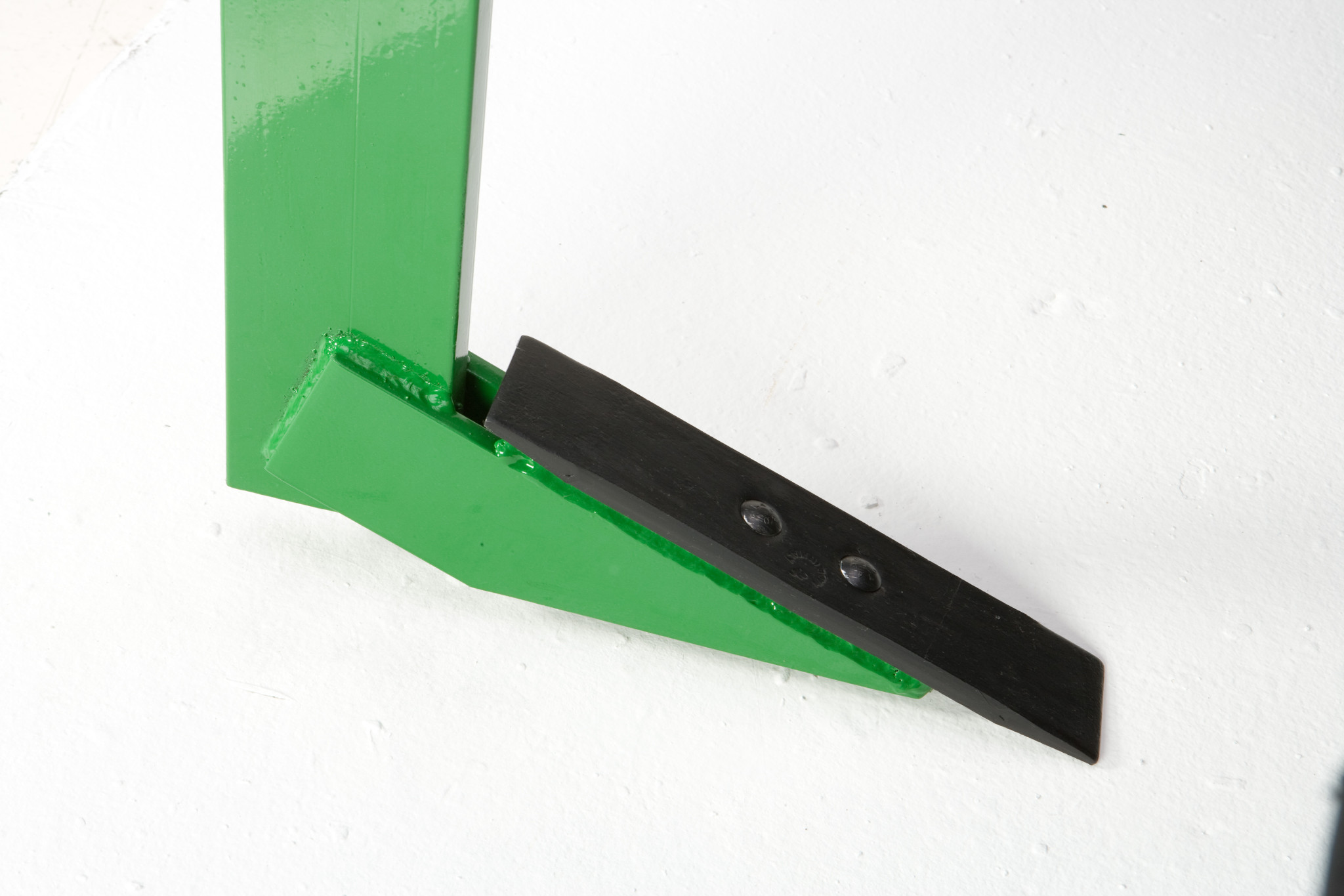 Close-up of a green shank with a black replaceable point bolted to the tip, resting on a white surface