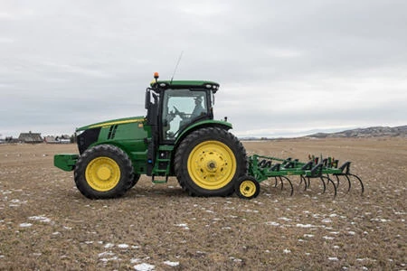 Side left view of a cab tractor pulling a 610 chisel plow across a snow-flecked, brown field
