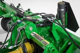 Close-up of a green tedder implement showing hydraulic valves, hoses, fittings, and protective shielding near the drivetrain
