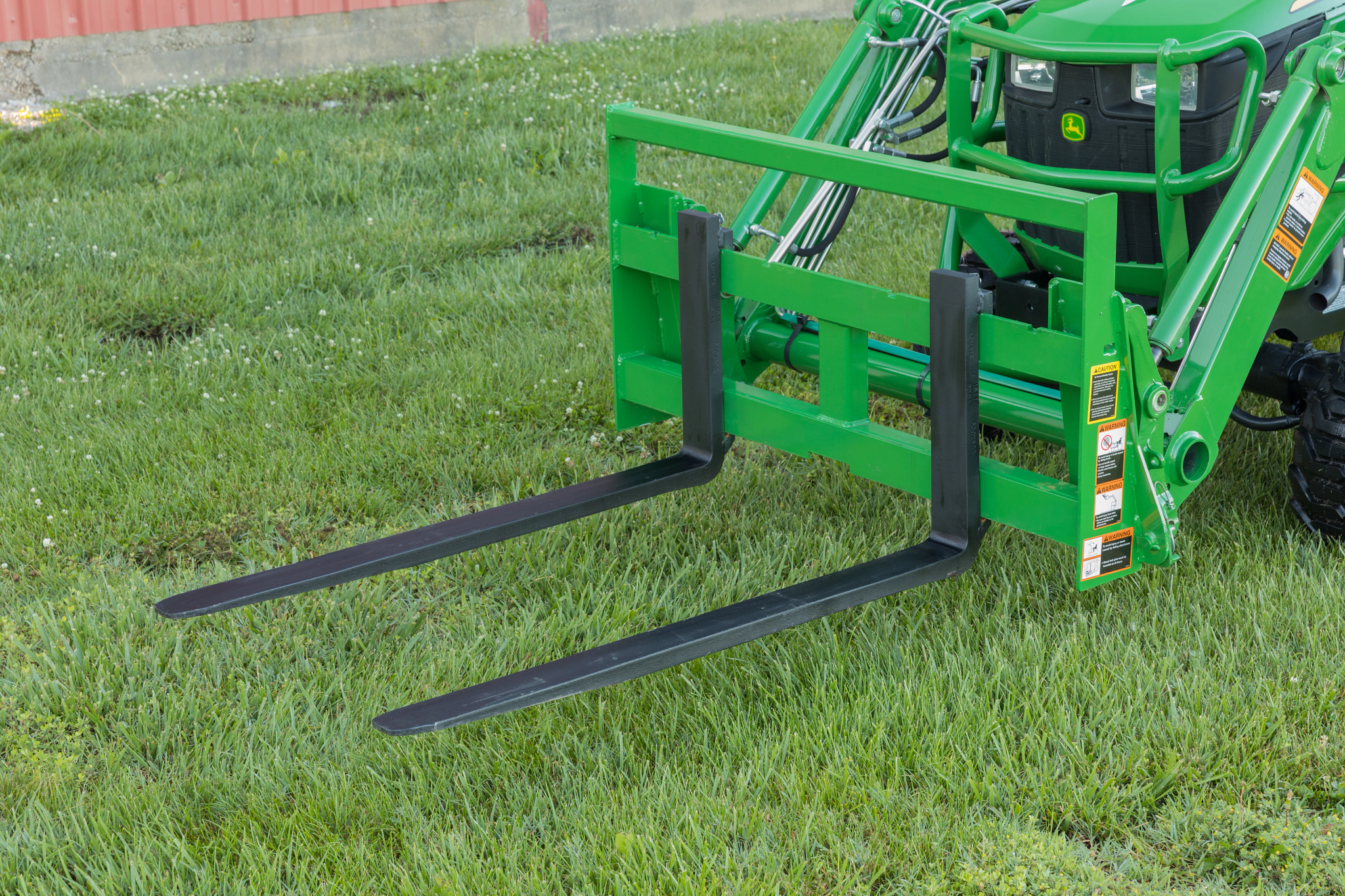 Front left view of a 1025R Sub-Compact Tractor on grass with attached AP11F Pallet Fork