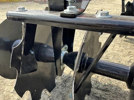 Close‑up of a black agricultural disc assembly showing multiple scalloped steel blades mounted on a horizontal axle, secured with metal brackets, bolts, and spacers.
