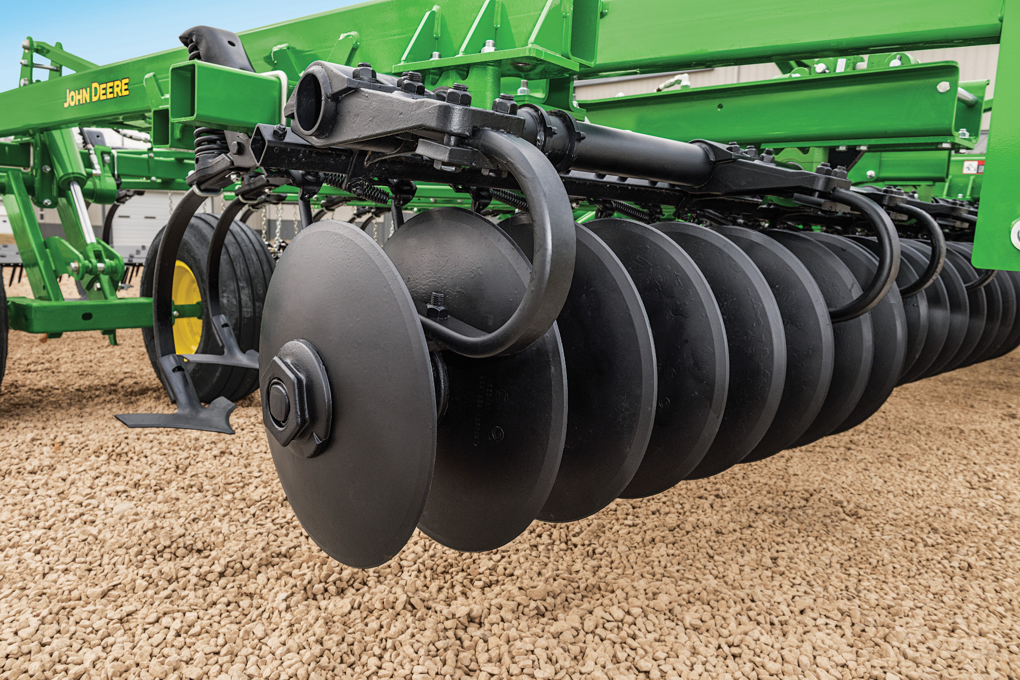 Close-up of a row of smooth black disc blades mounted on a green mulch finisher implement, shown over a gravel surface