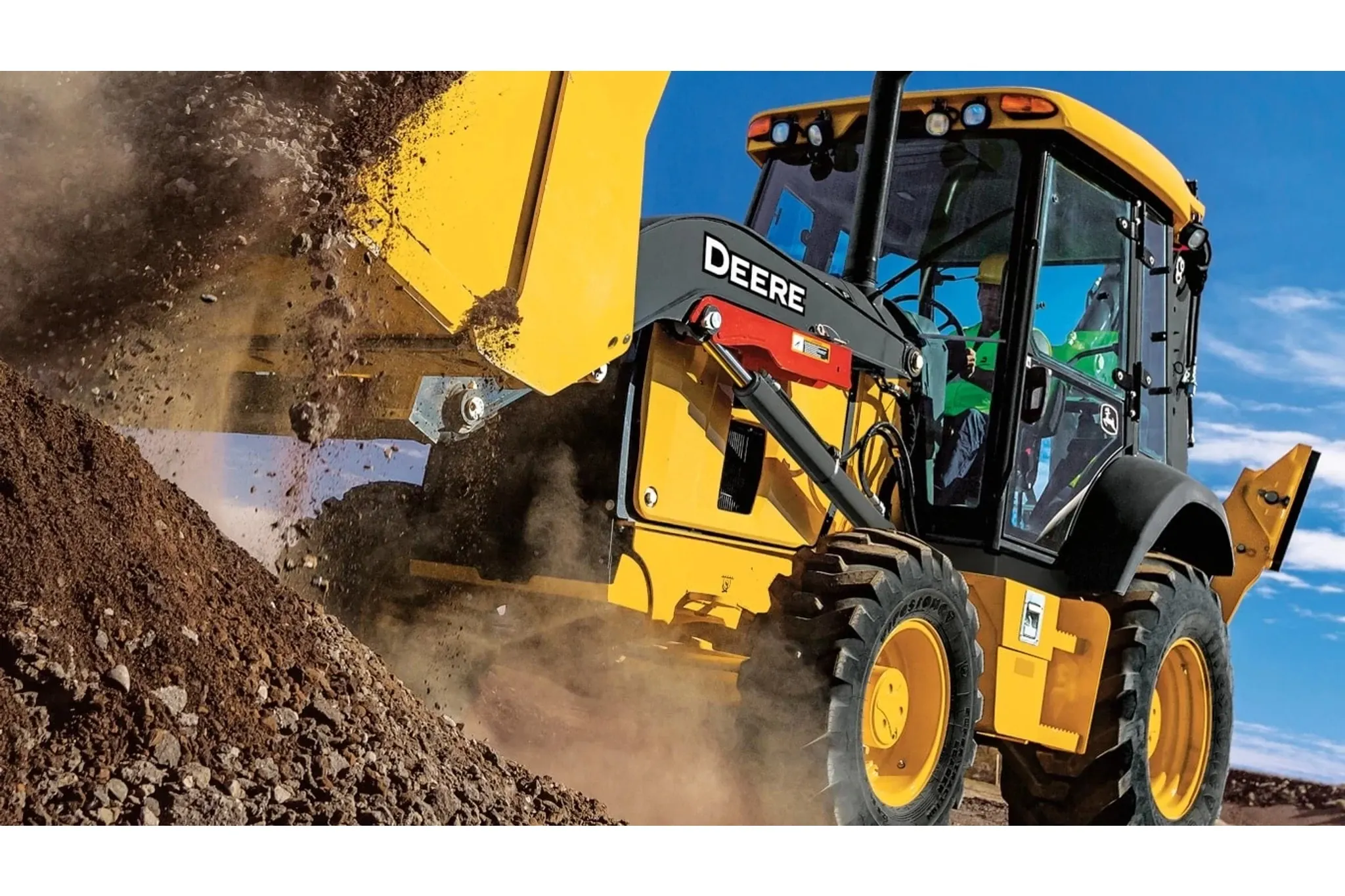 310 G-Tier Backhoe Loader dumping dirt and gravel into a large pile