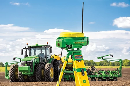 Front view of a StarFire™ 7500 on a yellow tripod with antenna in the foreground of a tractor in a field
