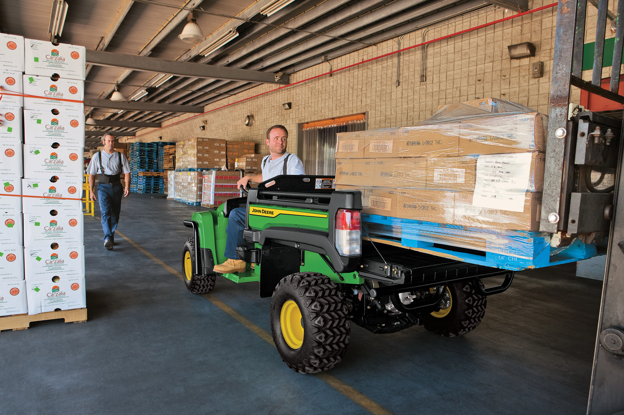 Rear left view of a TX 4x2 Gator with cargo box full of boxes being backed up to a truck in a warehouse