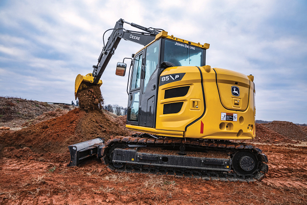 John Deere 85 P compact excavator working on a dirt construction site, featuring a yellow and gray body, enclosed cab, and metal tracks