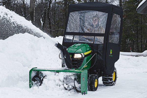 Front left view of an operator inside a weather enclosure on an X350 Tractor clearing a snowy driveway with a 44-in. Snow Blower and tire chains