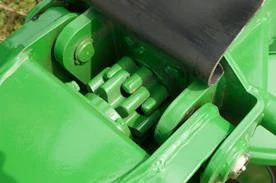 Close‑up of an agricultural machine hinge joint, showing interlocking metal components, pivot pins, and grease points beneath a protective metal panel.