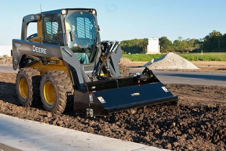 Skid steer loader equipped with a front grading attachment leveling soil at a construction site.