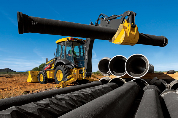 310 P-Tier Backhoe lifting a long black pipe at a dusty outdoor worksite