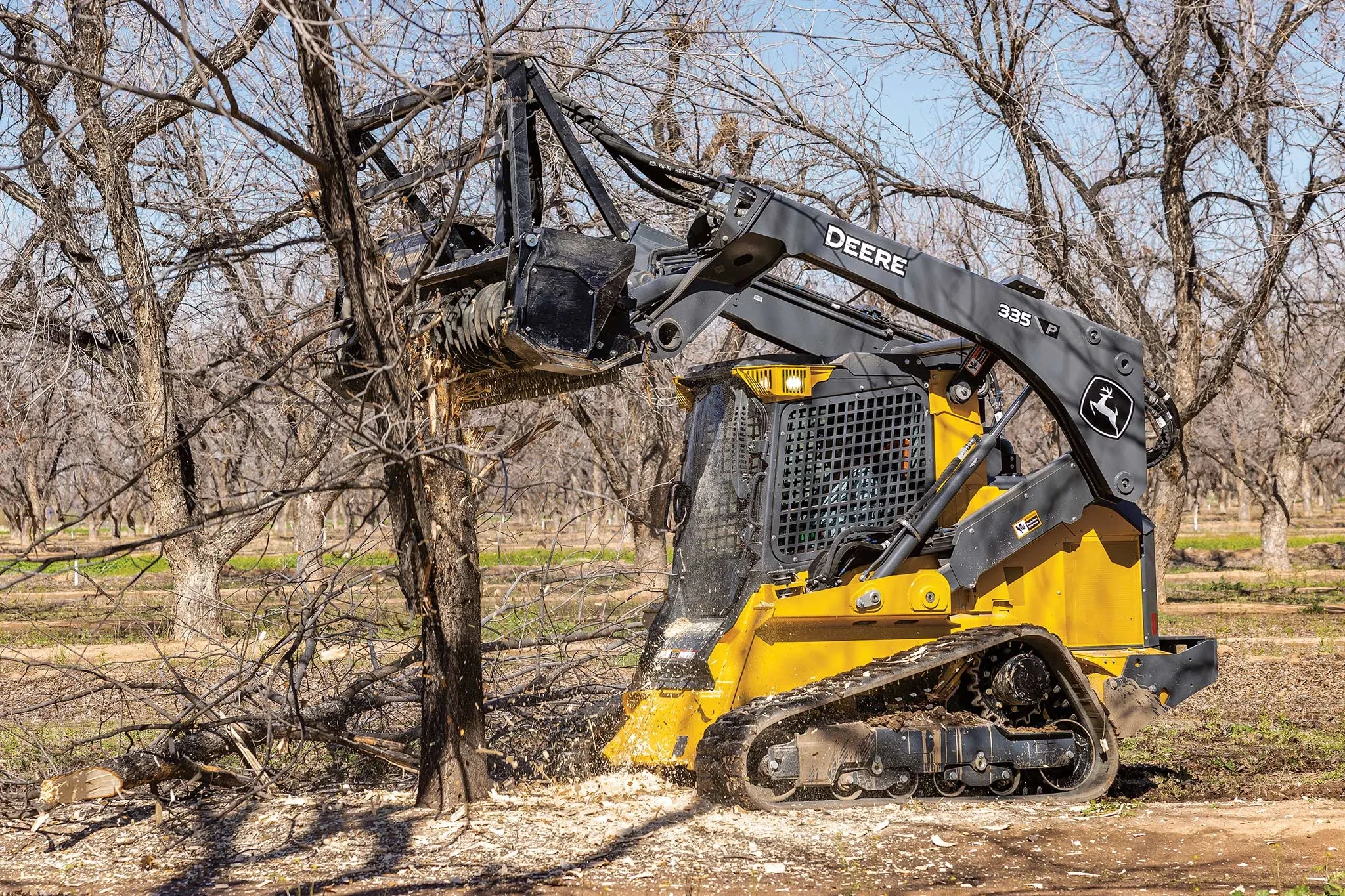 Side left view of a 335 P-Tier compact track loader grinding a tree with an MK76 mulching head