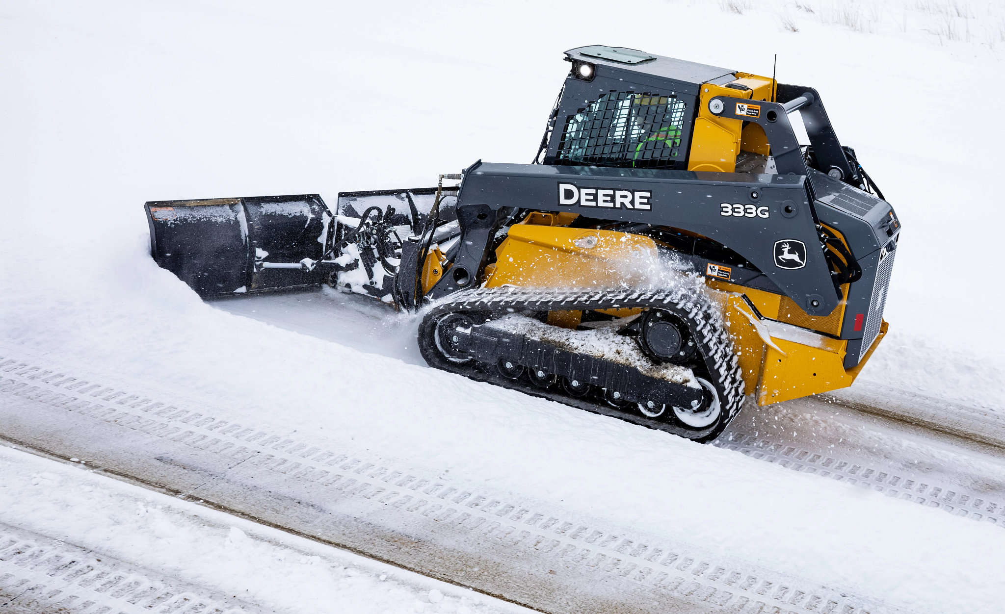 Side left view of a 333G Compact Track Loader pushing snow from a road with a BV9 V Blade attachment