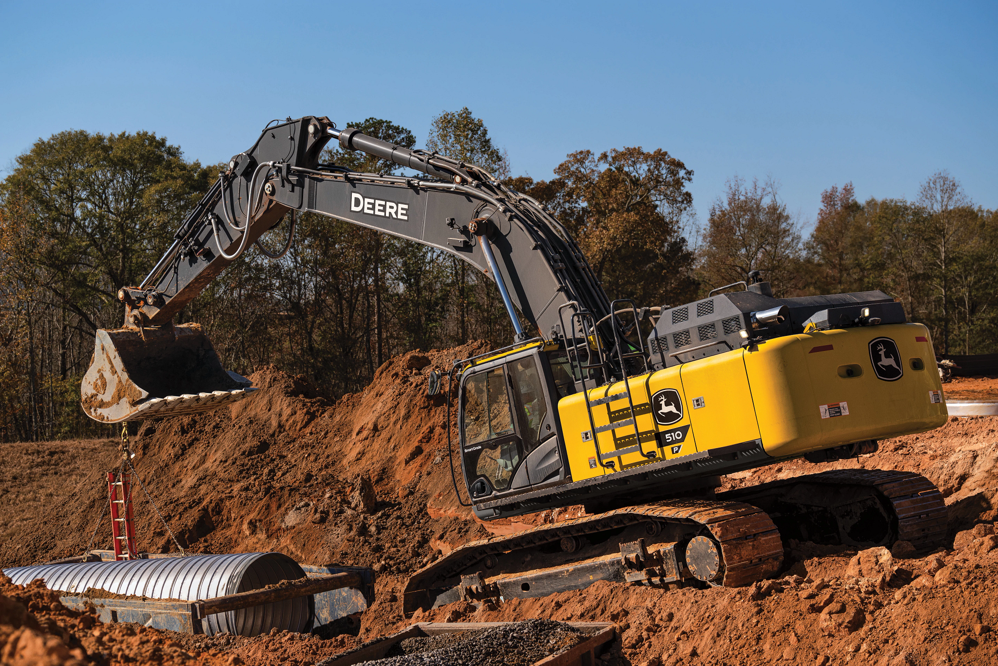 John Deere excavator operating on a dirt construction site, featuring a yellow and gray body, enclosed cab, and metal tracks