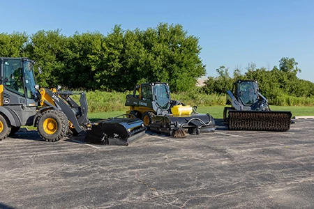 Front view of skid steers and a loader lined up on pavement with BA96C angled broom, BP84C Pick-Up Broom, and BP84C Pick-Up Broom attachments
