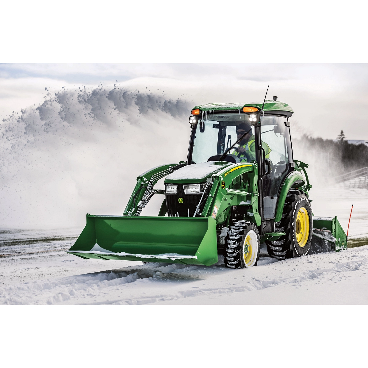 Front left view of a green 3046R compact utility tractor with 320R loader attachment snow blowing a road with rear-attached SB1164P snowblower Front left view of a green 3046R compact utility tractor with 320R loader attachment snow blowing a road with rear-attached SB1164P snowblower