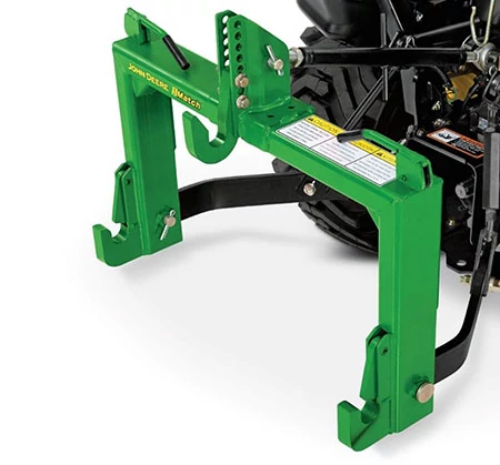 Green three-point hitch attachment mounted at the rear of a compact tractor, showing adjustable mounting hooks and hardware