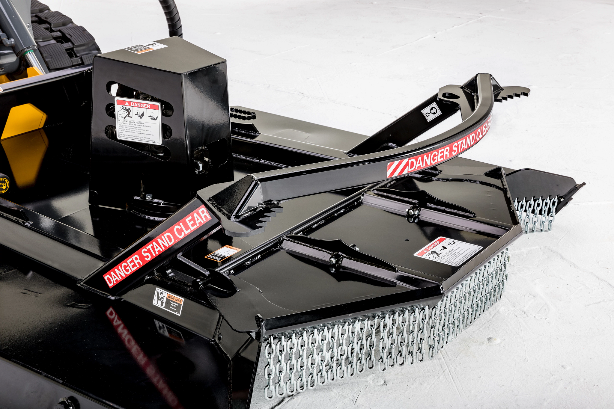 Black rotary mower attachment with twin cutting decks, chain curtains, and articulated arms labeled “DANGER STAND CLEAR”.
