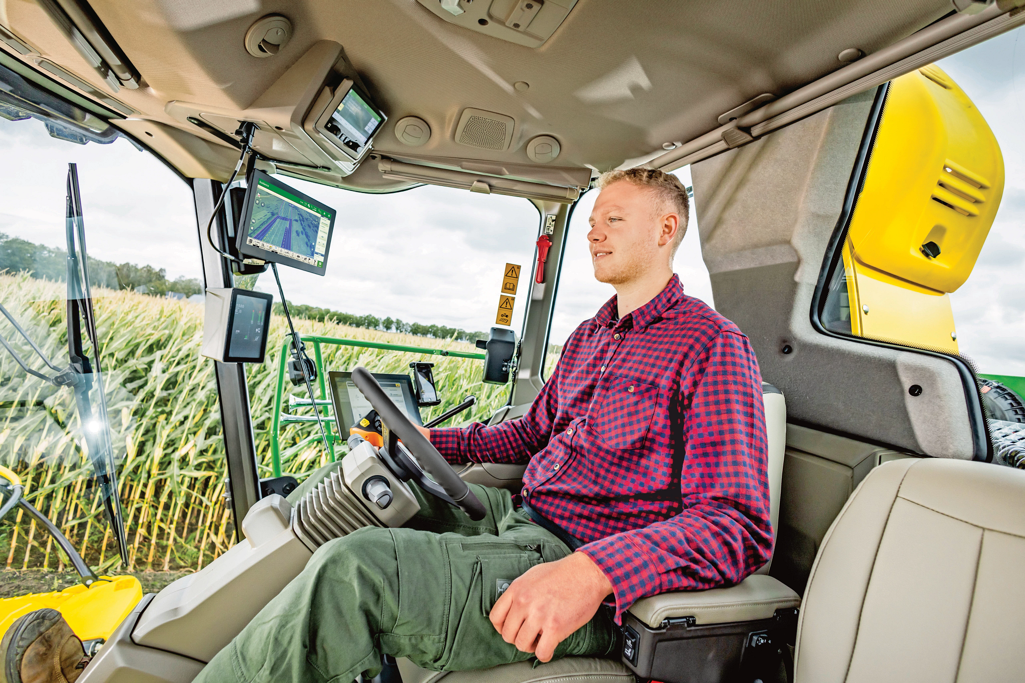 Individual sitting in the cab of a combine with a steering wheel in front of them.