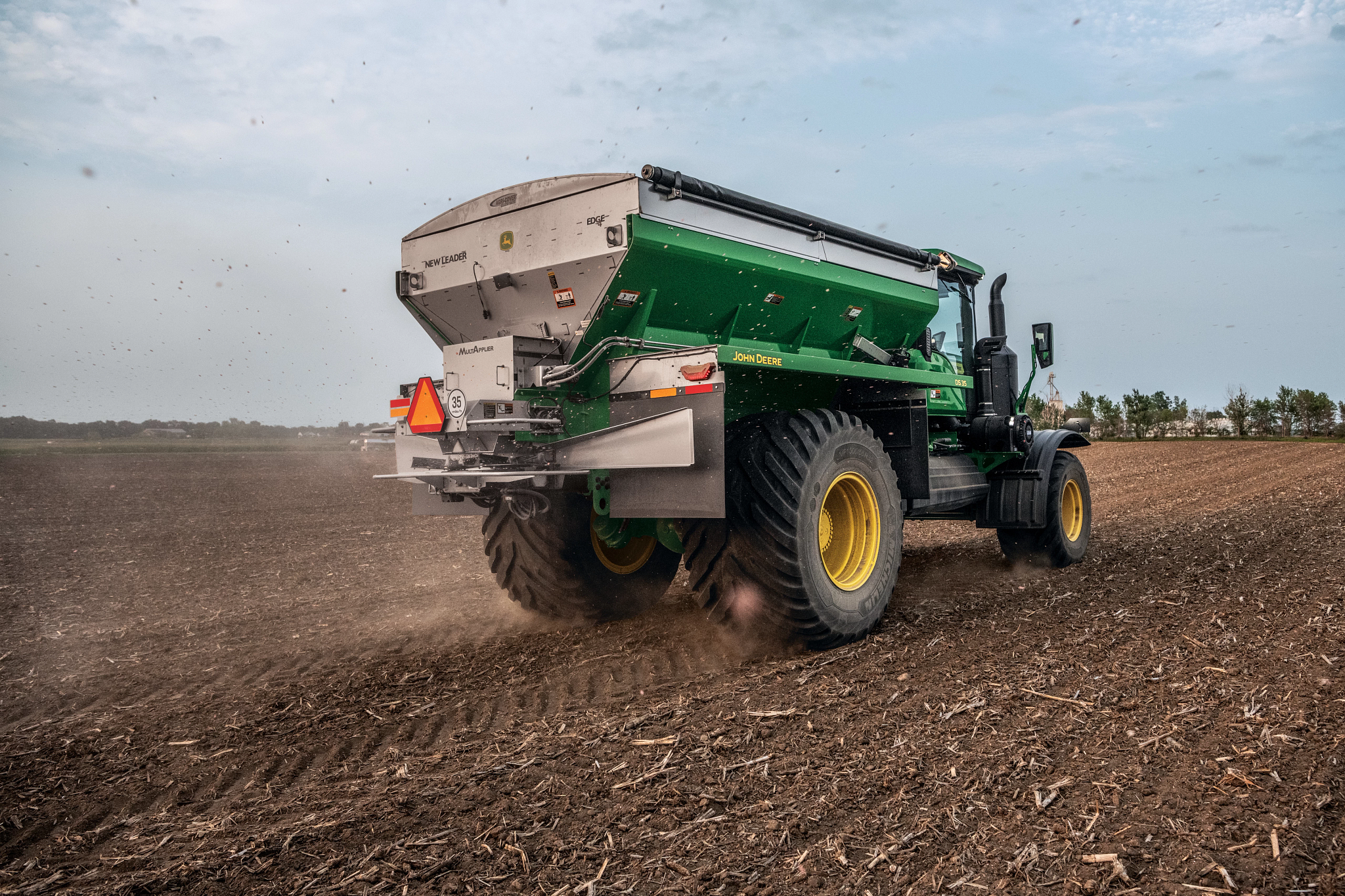 A green 800R Floater with attched DS35 Dry Spreader Box kicks up dust as it operates in a crop field.