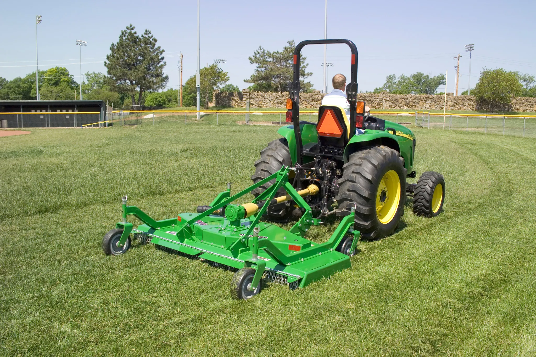 Rear right view of a John Deere tractor pulling a green GM2190R grooming mower on a sports field