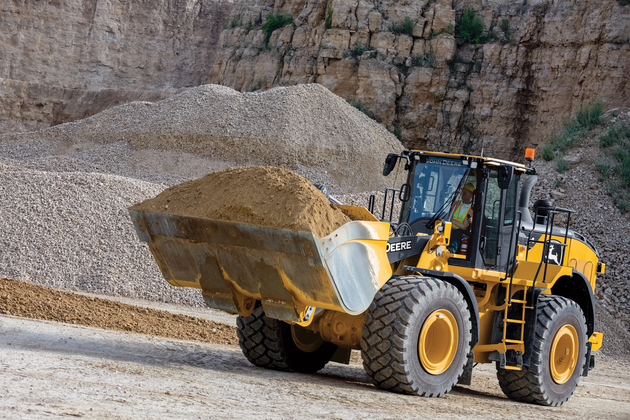 A large yellow front-end loader carries a full bucket of sand or fine gravel across a quarry floor