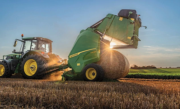 Round baler releasing a bale into a field at twilight